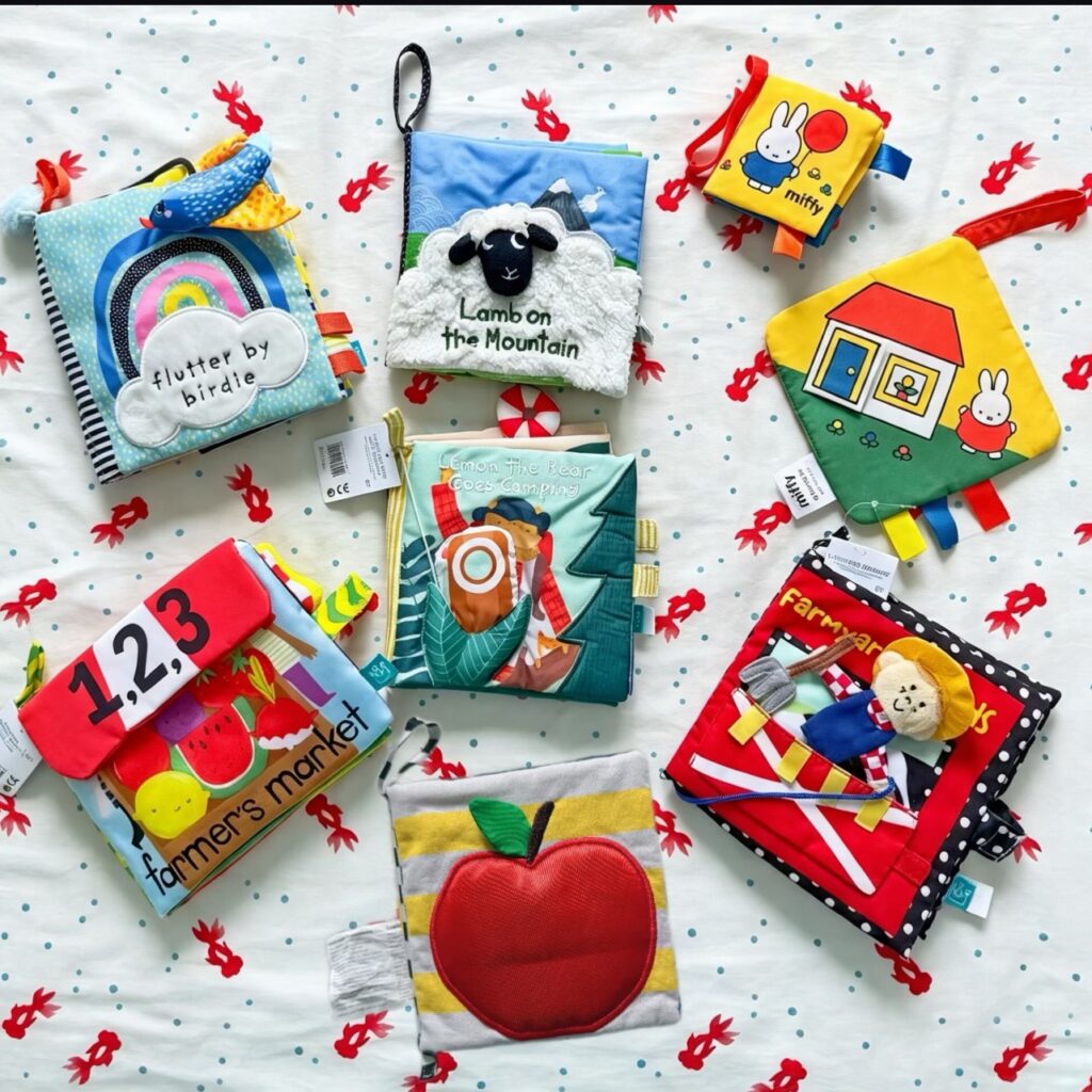 Collection of colorful interactive cloth books for babies, featuring animal and alphabet designs.